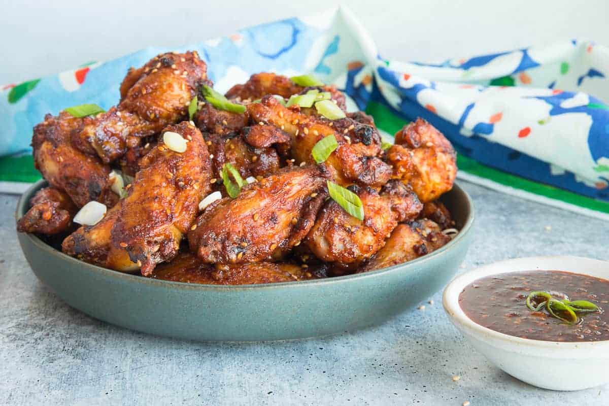 Horizontal image of the Gochujang Air Fryer Chicken Wings in a green bowl next to a ivory colored bowl filled with the sauce. 