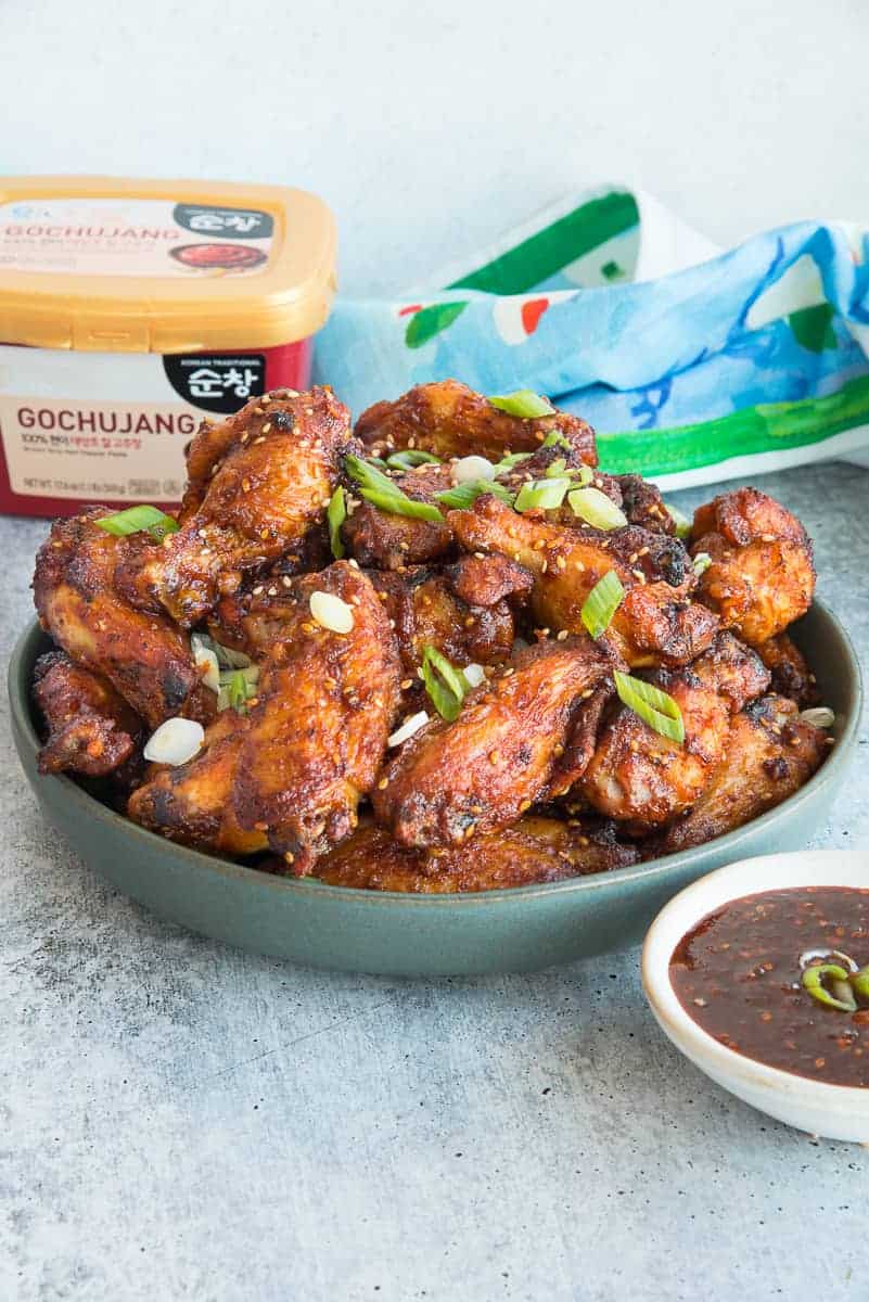 Portrait image of the Gochujang Air Fryer Chicken Wings in a dark green bowl garnished with sliced green onions and sesame seeds. 