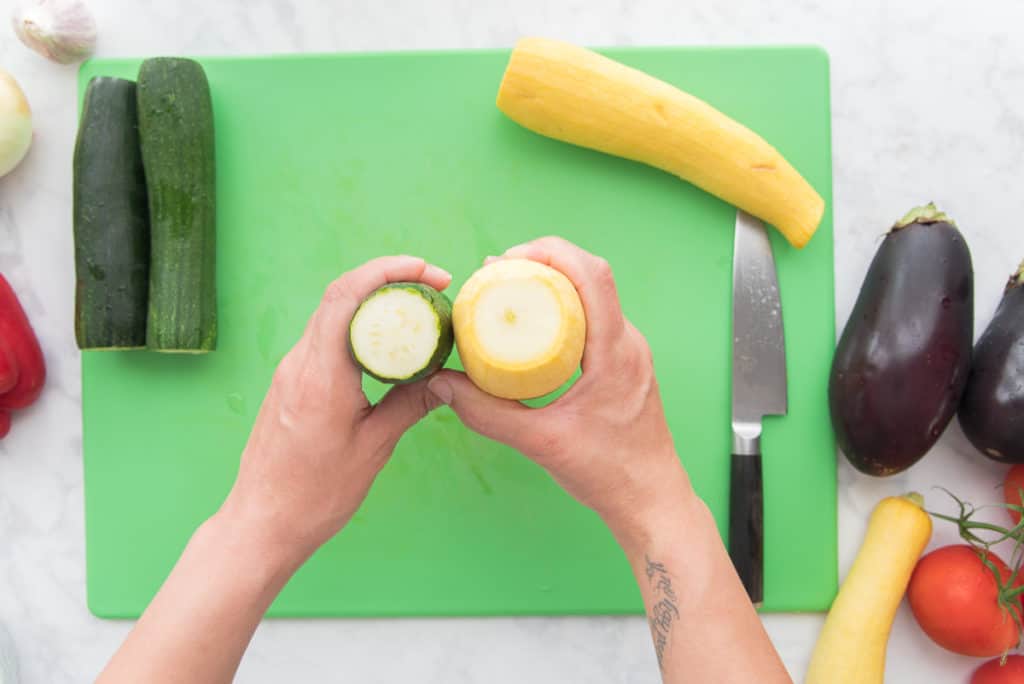 Two hands hold up a zucchini (left) and a yellow squash (right) to display the differences in circumference.
