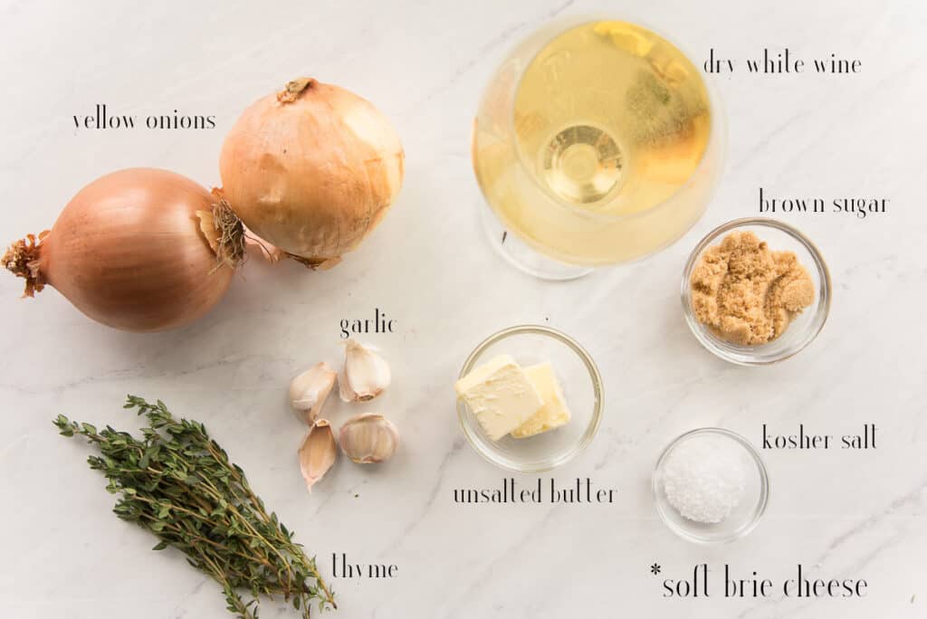 Ingredients to make Baked Brie Topped with Caramelized Onions: onions, dry white wine, brown sugar, salt, thyme, garlic, butter on a white surface