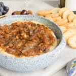 Preview Image of a blue baking dish with Baked Brie topped with Caramelized Onions surrounded by fresh fruits and baguette chips.