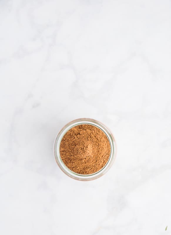 A small jar filled with Pumpkin Pie Spice Blend on a white marble surface.