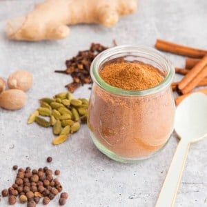 Pumpkin Pie Spice Blend in a glass tulip jar surrounded by whole spices.
