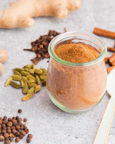 Pumpkin Pie Spice Blend in a glass tulip jar surrounded by whole spices.