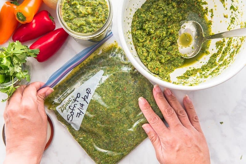 A hand seals a freezer bag filled with sofrito