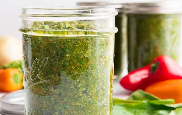A close up image of a jar of Sofrito surrounded by its ingredients and two more jars