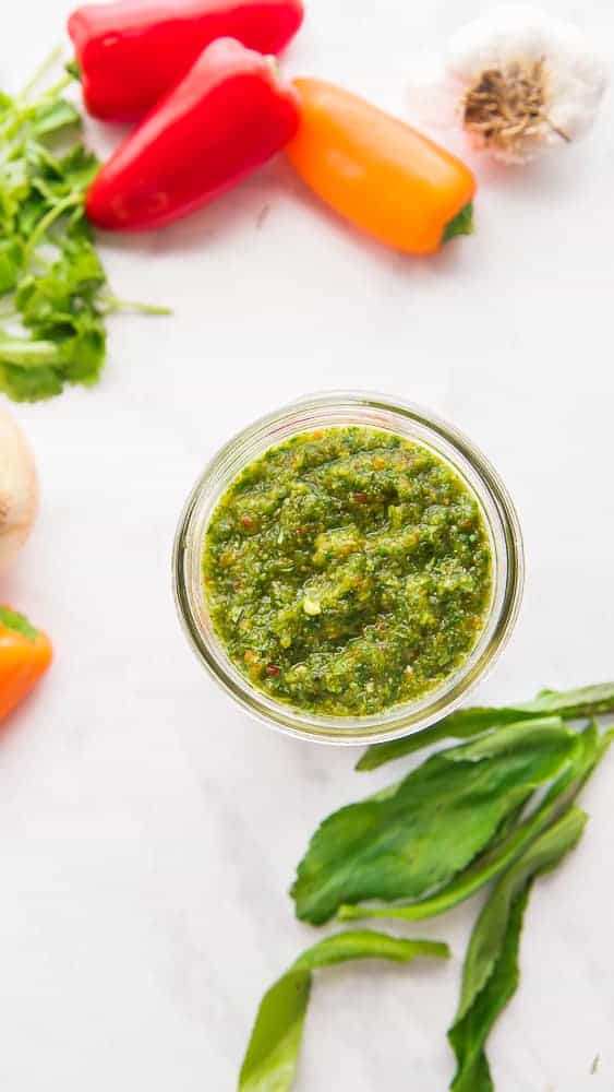 A jar of Sofrito is surrounded by the ingredients used to make it.