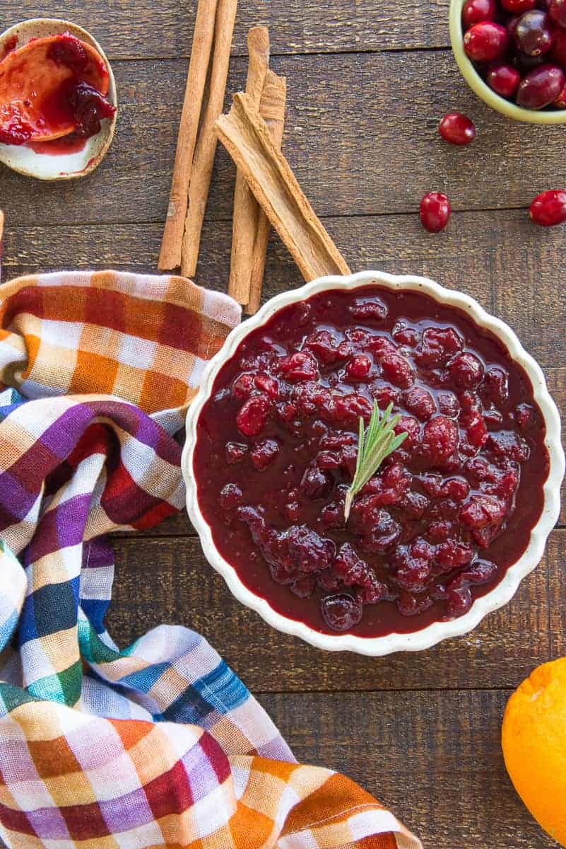 Lead image of a light-colored bowl filled with Boozy Spiced Cranberry Sauce surrounded by the rest of the ingredients in the recipe.
