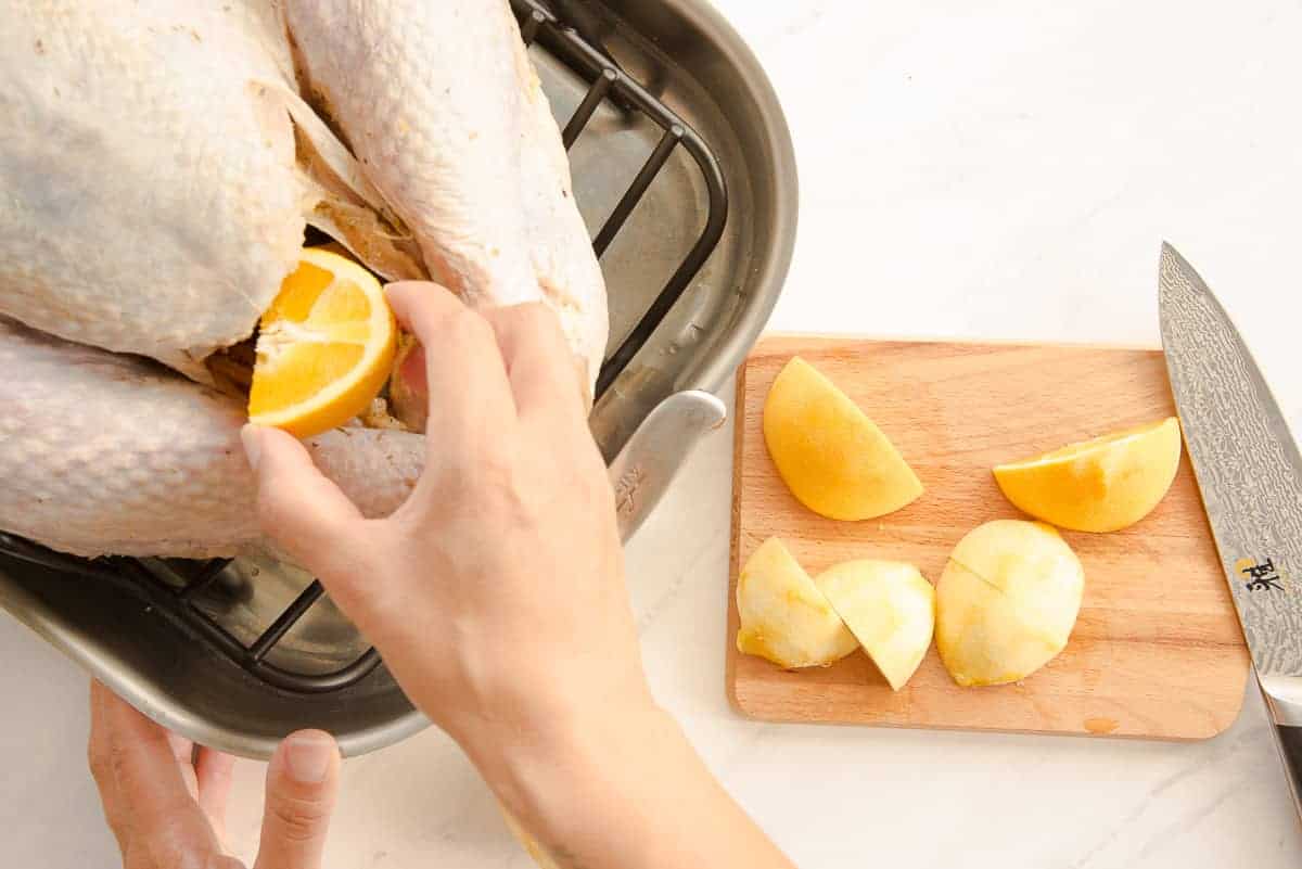 Hand inserts orange wedges into the cavity of the turkey before roasting.