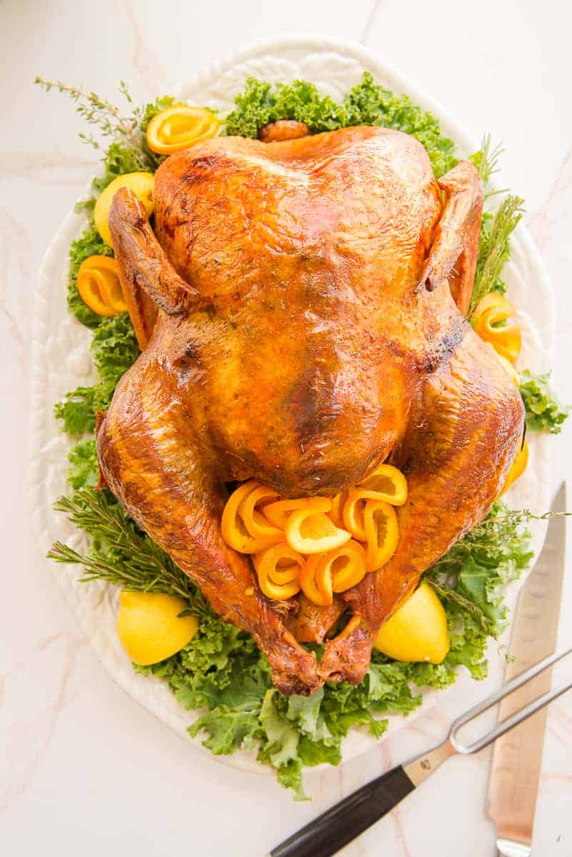 Lead image for How to dry brine and roast a turkey, turkey on a white platter on a bed of greens.