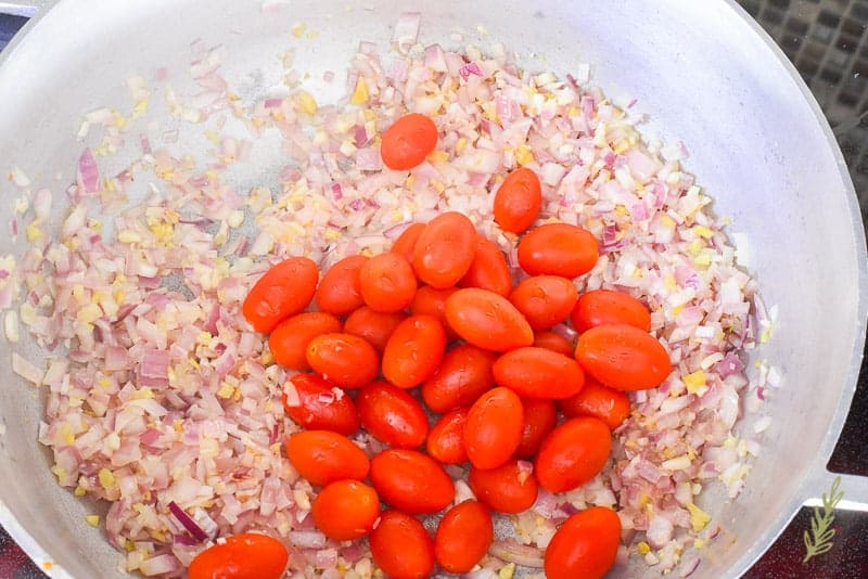 Cherry tomatoes are added to a pot of sauteed aromatics. 