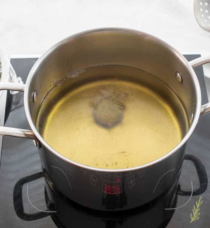 The falafels are deep fried in oil in a large silver pot