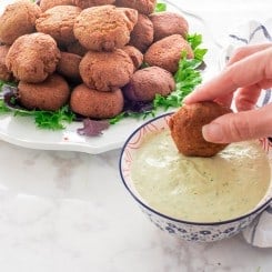 A hand dips an Egyptian Falafel into a bowl of tahini sauce