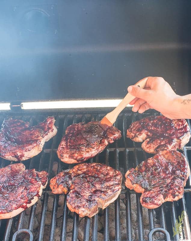 A hand uses a brush to cover grilled pork chops in the Blueberry Balsamic BBQ Sauce