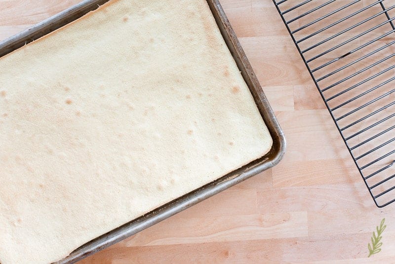 The baked sponge cake is on a sheet pan next to a cooling rack