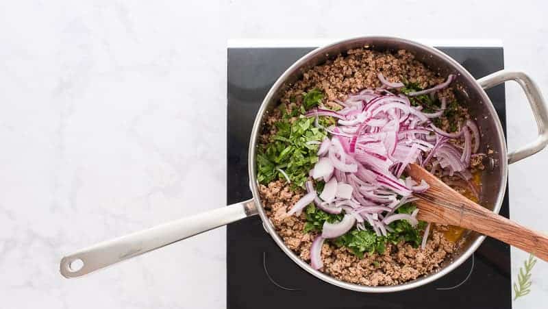 Red onions are thinly sliced and added to the Larb Moo in the pan with the herbs.