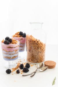 The Honey Almond Granola in a jar with two glasses of granola parfait to the right. 