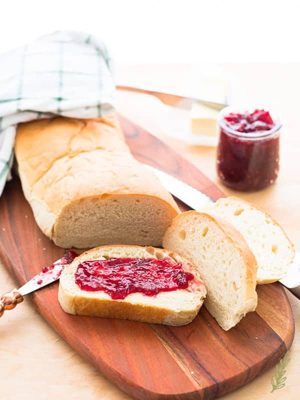 A loaf of Pan Sobao is sliced. One slice has red jam spread over it