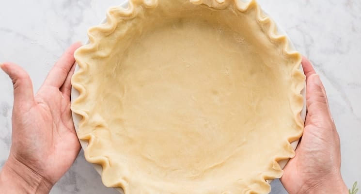 Mealy pie dough in a pie plate held by two hands.