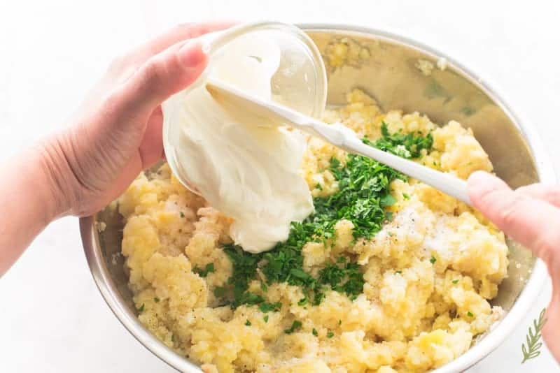 The cream, herbs, and sour cream are added to the silver bowl of Rustic & Rich Mashed Potatoes