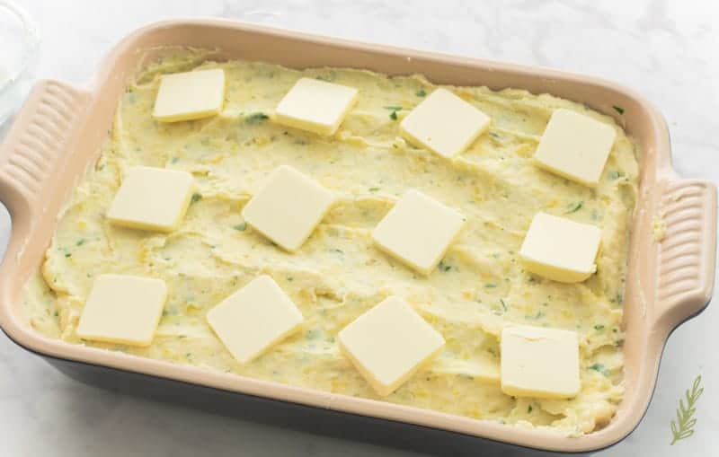 Pats of butter are placed onto the surface of the Rustic & Rich Mashed Potatoes