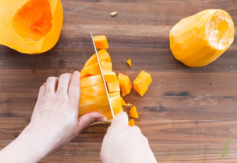 A knife is used to cut the Butternut Squash on a dark, wooden surface.