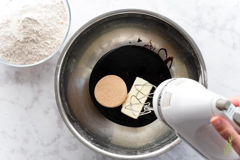 Molasses, butter, and brown sugar are combined in silver mixing bowl with a white hand mixer.