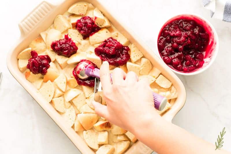 A hand scoops boozy spiced cranberry sauce onto the casserole.
