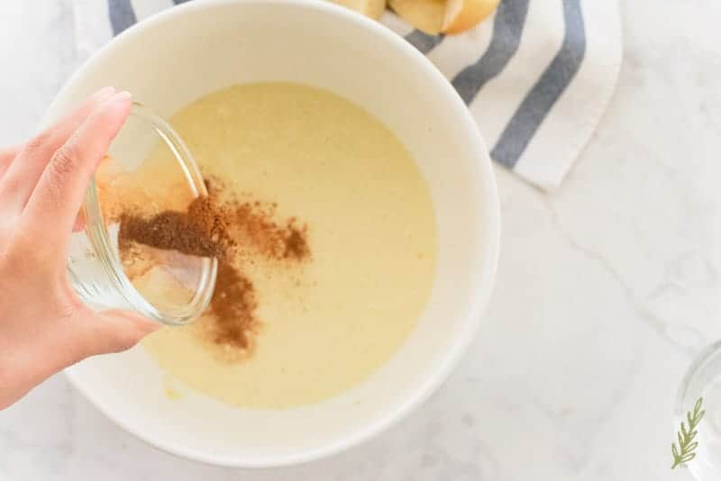 A spice blend is added to the custard in a white ceramic bowl