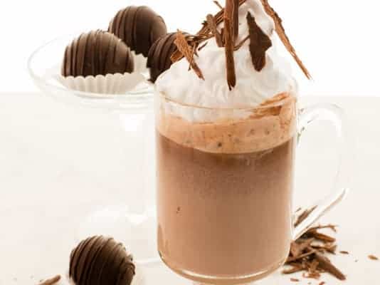 A glass of Original Truffle Hot Chocolate surrounded by other truffles and shaved chocolate