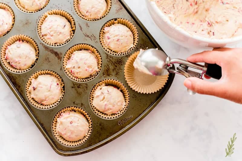 The Vanilla-Cranberry Muffin is scooped into a muffin tin lined with brown paper cups. 