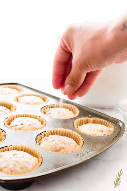 A hand sprinkles the spiced-sugar over the scooped Vanilla-Cranberry Muffin batter before baking.