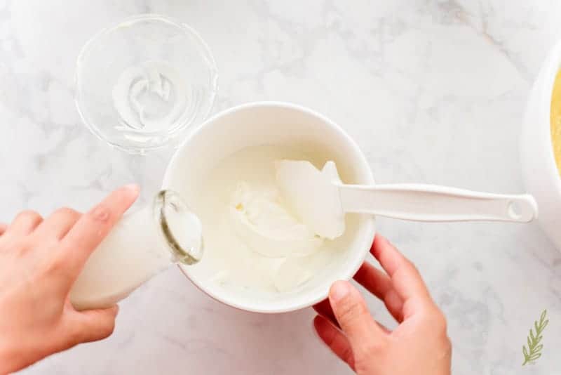 Cream is added to a white mixing bowl filled with the rest of the wet ingredients.