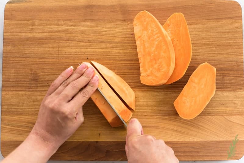 And uses a knife to cut sweet potatoes into slabs on a wooden cutting board