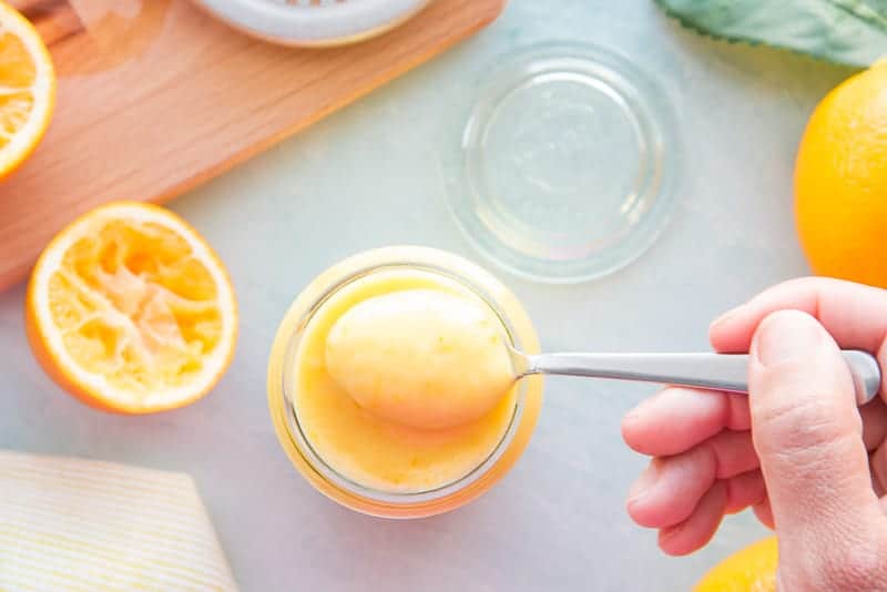 A silver spoon lifts the Meyer Lemon curd from a small glass jar.