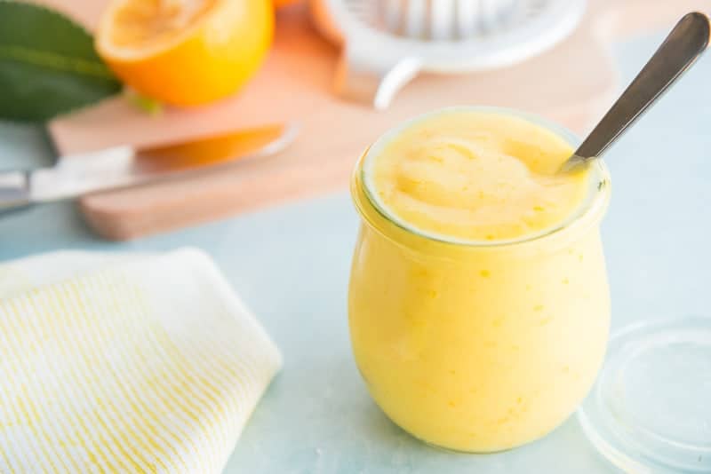 A small glass jar of Meyer Lemon Curd with a silver spoon in it