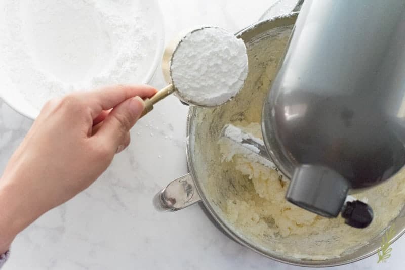 Powdered sugar is being added on the left side of the mixer to the bowl with the butter.