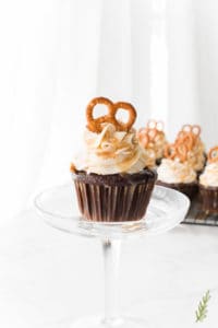 A single Chocolate Stout-Pretzel Cupcake with Bailey's Buttercream and Caramel Drizzle with more cupcakes in background