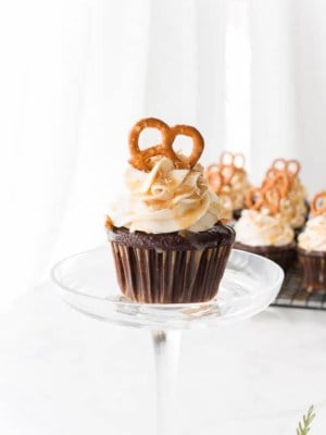 A single Chocolate Stout-Pretzel Cupcake with Bailey's Buttercream and Caramel Drizzle with more cupcakes in background