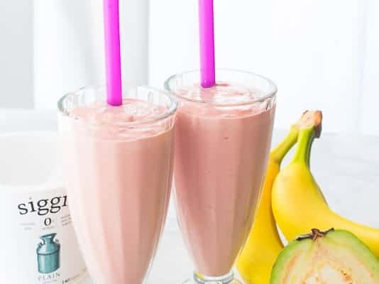 Two glasses of Guava Banana Oatmeal Breakfast Shake are surrounded by their ingredients.