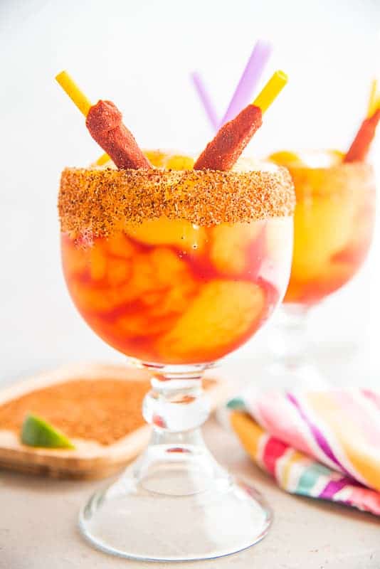 two mangonadas in schooner glasses rimmed with tajin and garnished with tamarind-chile straws.