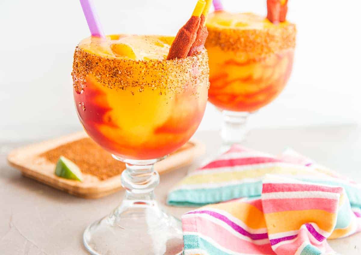 Two goblets filled with Mangonada (Spiced Mango Margarita) a grey surface