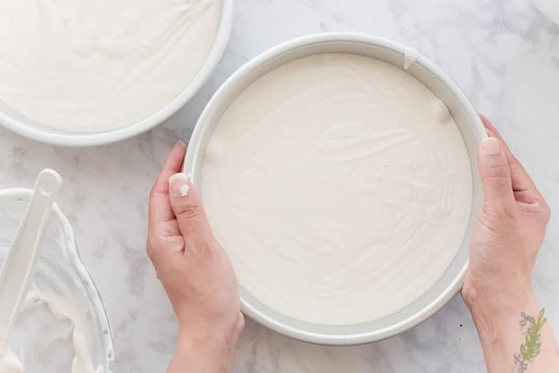Two hands tap the pan gently against the countertop to release any air bubbles from the cake batter