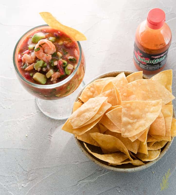Overhead shot of Coctel de Camarones (Mexican Shrimp Cocktail) in large goblet with tortilla chips and Mexican hot sauce.