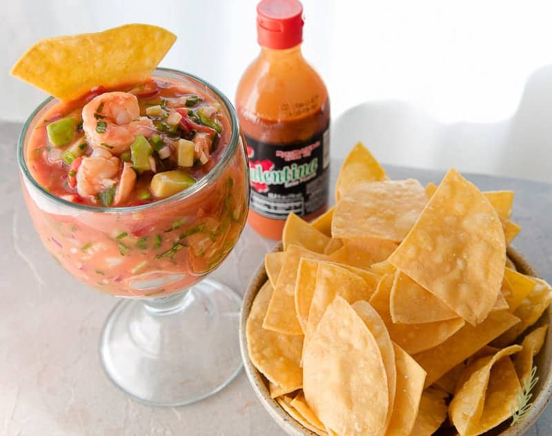 Three-Quarter angle shot of Coctel de Camarones (Mexican Shrimp Cocktail) in large goblet with tortilla chips and Mexican hot sauce.