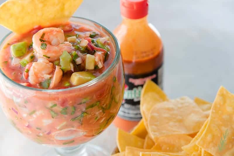 Close up shot of Coctel de Camarones (Mexican Shrimp Cocktail) in large goblet with tortilla chips and Mexican hot sauce.
