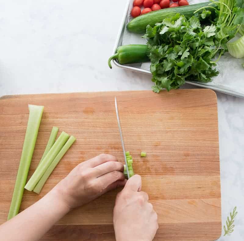 Dicing celery stalks with chef's knife on cutting board for Coctel de Camarones (Mexican Shrimp Cocktail)