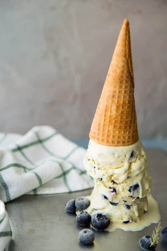 Cone with three scoops of Kaffir Lime and Blueberry Frozen Custard upside down on sheet pan with blueberries surrounding
