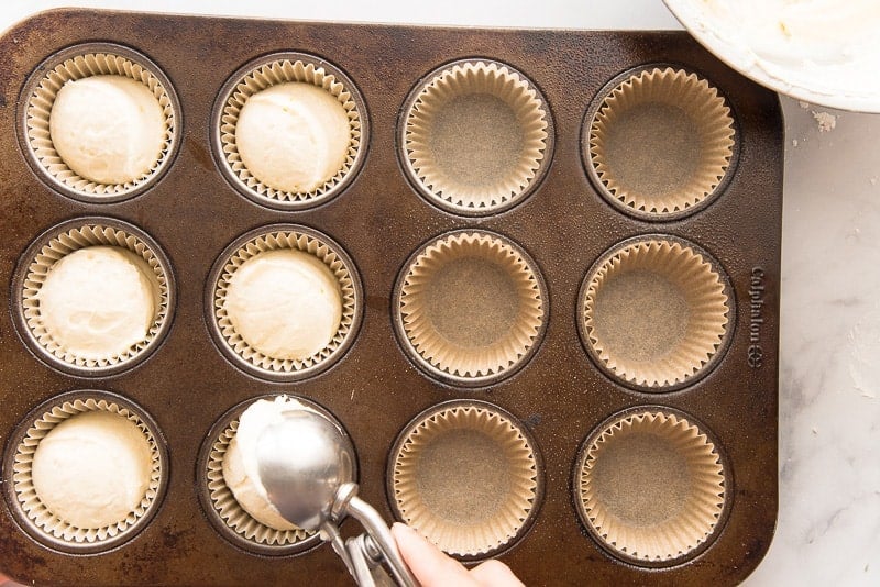 A portion scoop drops the batter into a paper-lined muffin tin.