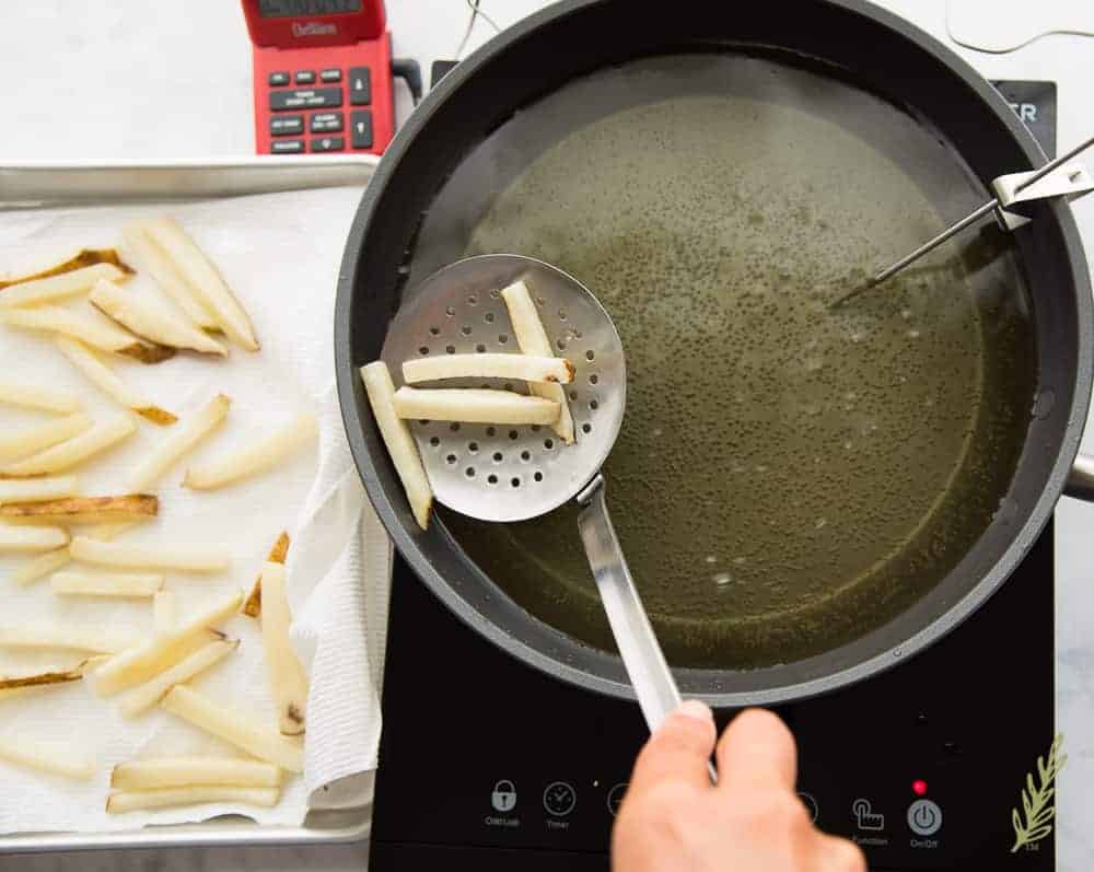 Removing fries from the oil after the first fry.